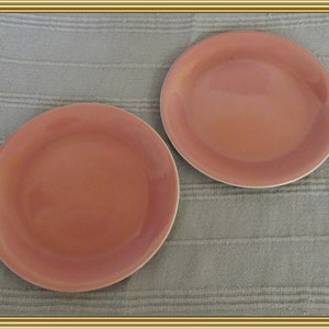 May include: Two terracotta colored ceramic plates on a textured beige surface.