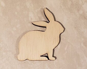 May include: A wooden cutout of a rabbit in a sitting position. The rabbit is made of light brown wood and has a simple, minimalist design.