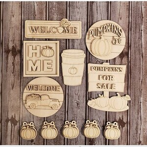 May include: A set of 12 unfinished wooden cutouts featuring fall-themed designs. The cutouts include signs that say "Welcome", "Home", "Pumpkins for Sale", and "Pumpkins 5c". There are also cutouts of a coffee cup, a truck, and pumpkins.