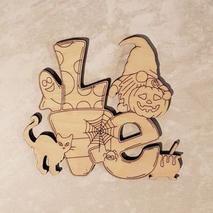 May include: Wooden cutout of the word "Love" decorated with Halloween themes. The "L" has a ghost and polka dots, the "O" has a spider web and spider, the "V" has a pumpkin wearing a hat, and the "E" has a black cat.