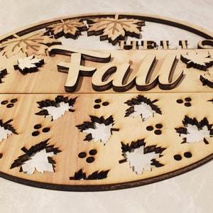 May include: A round wooden sign with the words "Hello Fall" in a decorative font. The sign is decorated with cut-out leaves and berries.