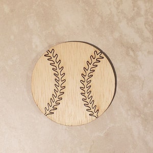 May include: A wooden coaster with a baseball design. The baseball is outlined in black and has a stitched pattern.
