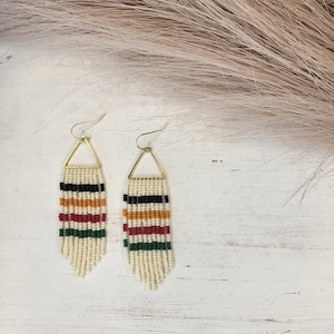 May include: A pair of gold triangle dangle earrings with white, black, red, orange, and green beaded fringe.