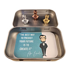 May include: A silver, gold, and bronze metal bust of Abraham Lincoln in a tin box with a quote from him that reads "The best way to predict your future is to create it."