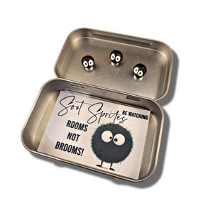 May include: A silver tin with a black and white illustration of a soot sprite with the text "Soot Sprites Be Watching Rooms Not Brooms!"  Three black soot sprite magnets are inside the tin.