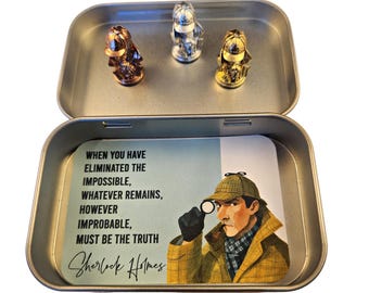 May include: A rectangular metal tin containing three small metallic detective figurines in copper, silver, and gold tones. Inside the lid, a card features an illustration of Sherlock Holmes with a magnifying glass and the quote: When you have eliminated the impossible, whatever remains, however improbable, must be the truth.