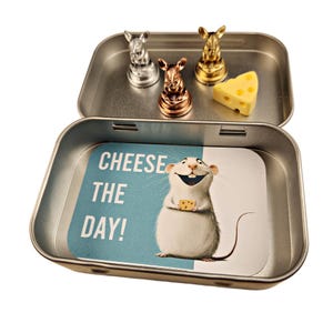 May include: A silver tin with a blue and white card inside that says "Cheese the Day!"  The tin has three silver, gold, and copper mice figurines on the lid.  A small wedge of cheese is also on the lid.