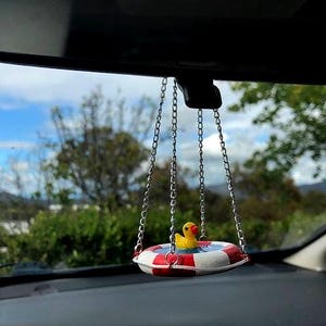May include: A yellow rubber ducky in a red, white, and blue life preserver hanging from the rearview mirror of a car.