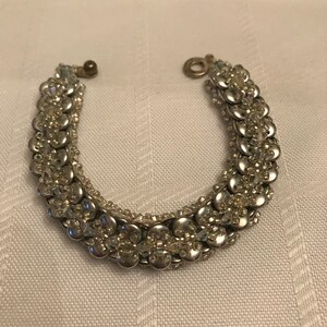 K&ouml;nnte beinhalten: Ein silbernes Armband mit einem Verschluss. Das Armband besteht aus kleinen, runden Perlen, die in einem Muster angeordnet sind. Die Perlen sind silberfarben und haben eine gl&auml;nzende Oberfl&auml;che.