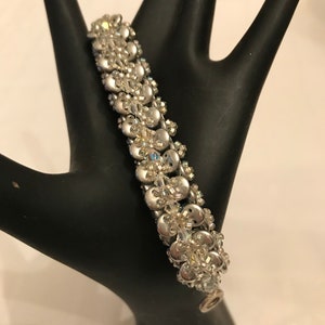 K&ouml;nnte beinhalten: Ein silbernes Perlenarmband mit klaren Kristall-Akzenten. Das Armband ist aus kleinen, runden Perlen gefertigt und hat einen zarten, femininen Look.