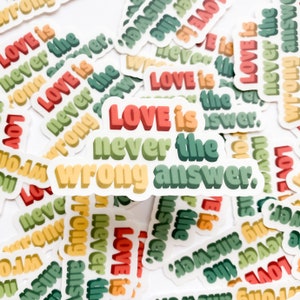 May include: A close-up of several colorful stickers with the phrase "Love is never the wrong answer." repeated on each sticker. The stickers are arranged in a random pattern on a white background.
