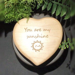 Puede incluir: Una caja de madera en forma de corazón con las palabras "You are my sunshine" y un sol con una cara grabada en ella.