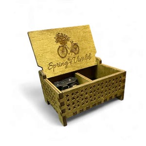 May include: A wooden music box with a carved design on the lid. The lid is open and shows a small music mechanism inside. The lid is engraved with a bicycle with flowers and the text "Spring Vivaldi".