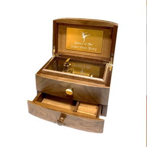May include: A wooden music box with a drawer and a glass lid. The lid is open and the music box plays the song "Dance of the Sugar Plum Fairy".