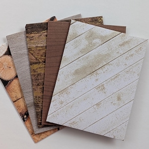 May include: A collection of decorative paper sheets with various wood grain patterns. The sheets display a range of colors, including light and dark browns, gray, and white. One sheet features a diagonal plank design.