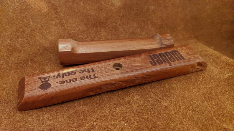 Pode incluir: Duas ferramentas de grelha de madeira com o texto "Weber" e "The one. The only." gravado na madeira. As ferramentas s&atilde;o de cor castanho m&eacute;dio e parecem novas.