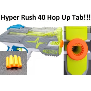 May include: A gray, blue, and neon green toy gun with the text "Hyper Rush 40 Hop Up Tab!!!" The gun has a clear top and an orange barrel. An orange and yellow accessory is shown in the lower left corner.