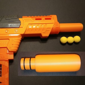 Könnte beinhalten: Eine orangefarbene und schwarze Spielzeugpistole mit einem abnehmbaren orangefarbenen Lauf und drei gelben Schaumstoffbällen. Die Pistole hat ein strukturiertes Design und ist vor einem dunklen Hintergrund platziert. Der Lauf ist zylindrisch mit schwarzen Ringen.