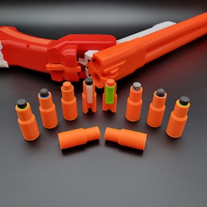 May include: A set of ten orange and black toy darts for a toy gun. The darts are made of plastic and have a rounded tip. The darts are arranged in a circle on a black surface.