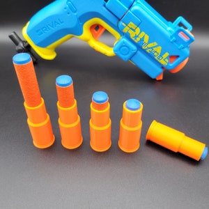May include: A blue and yellow toy gun with the word "Rival" on the side. There are six orange and blue foam darts in front of the gun.