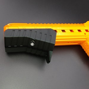Peut inclure: Un jouet pistolet noir et orange avec une poignée texturée. Le pistolet a une poignée noire avec une vis sur le côté.
