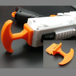 May include: A white and orange plastic toy gun with a black handle and an orange trigger. The gun has a white and black switch on the side. The gun is designed to be used with darts.