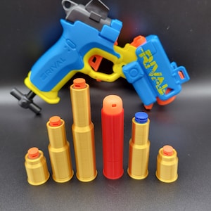May include: A blue and yellow toy gun with the word "Rival" on the side. There are six toy bullets in front of the gun, five are gold and one is red.