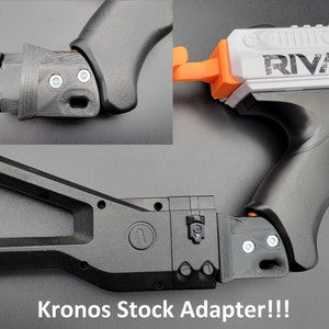May include: Black plastic stock adapter for a Nerf Rival Kronos blaster. The adapter has a textured surface and a small, round button on the side. The text "Kronos Stock Adapter!!!" is printed on the bottom of the image.