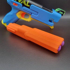 May include: A blue and yellow toy gun with the text "RIVAL" and an orange accessory. The accessory is orange with two purple tips. The toy gun is blue, yellow, and orange.