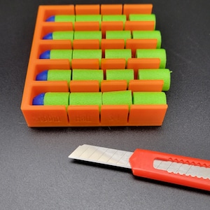 May include: Orange plastic storage case with green and blue foam darts. The case has labels that read "Small", "Half", and "3/4". A red utility knife is also in the image.