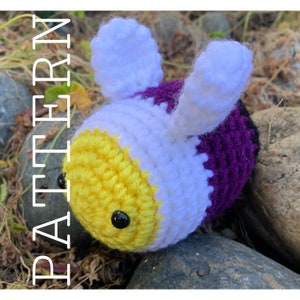May include: A crocheted bee plush toy with yellow, white and purple stripes. The bee has black eyes and white wings.