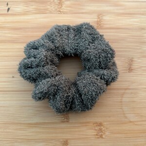 May include: A gray fuzzy scrunchie hair tie. The scrunchie is made of a soft, plush fabric.
