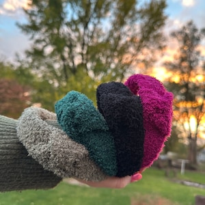 May include: Four fuzzy hair scrunchies in different colors: gray, green, black, and pink.