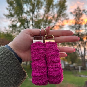 May include: Two pink fuzzy keychains with silver and gold metal rings. The keychains are made of a soft, fluffy material.