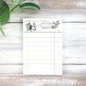 May include: A vintage-style notepad with a black and white illustration of a watering can and a banner that reads "J. Garrison & Sons Wholesale Seed Merchants 1901 Vivland St. Yorkshire, England For Gardens & Yield".