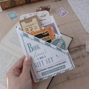 Peut inclure: Une enveloppe en papier triangulaire &eacute;tiquet&eacute;e Book lover's MINI GIFT SET STATIONERY BUNDLE FOR READERS LITERARY CRAFT PARLOUR contenant divers articles de papeterie dont un ticket beige, un petit sachet orange et un autocollant vert rond.