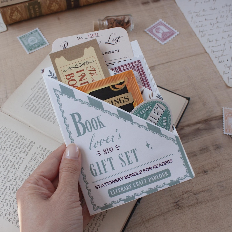 Peut inclure: Une enveloppe en papier triangulaire &eacute;tiquet&eacute;e Book lover's MINI GIFT SET STATIONERY BUNDLE FOR READERS LITERARY CRAFT PARLOUR contenant divers articles de papeterie dont un ticket beige, un petit sachet orange et un autocollant vert rond.