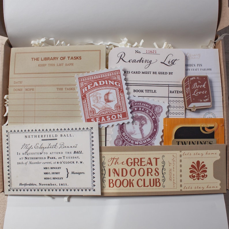 May include: A collection of paper stationery items in a box, including a Library of Tasks card, a Reading List card, a Netherfield Ball invitation, a Great Indoors Book Club ticket, a book-shaped pin, and a Twinings tea bag with vintage graphics.
