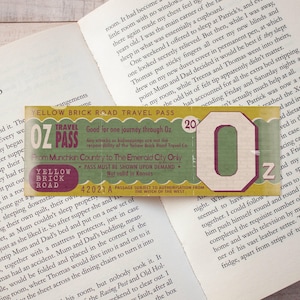 Peut inclure: Un ticket de voyage rectangulaire Yellow Brick Road aux tons verts et jaunes avec le texte OZ PASS, Good for one journey through Oz, From Munchkin Country to The Emerald City Only, et Not valid in Kansas, avec une grande lettre O et Z.