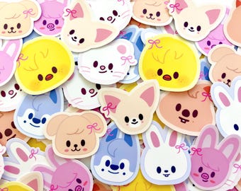 Op de afbeelding: Een verzameling kleurrijke stickers met schattige cartoon dieren. De stickers bevatten konijnen, kuikens, honden en andere wezens, elk met een schattig ontwerp en een strik. De stickers zijn in tinten roze, geel, blauw en beige.