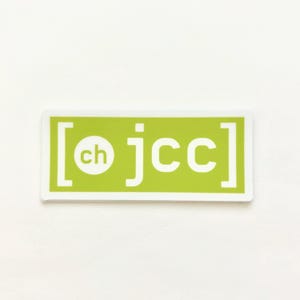 May include: A rectangular sticker with a white border and a light green background. The sticker features the letters "jcc" in white, with "ch" in a white circle. The text is enclosed in white brackets.