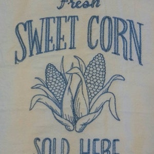 May include: White kitchen towel with blue embroidery that reads "Fresh Sweet Corn Sold Here". The embroidery also includes a depiction of three ears of corn.