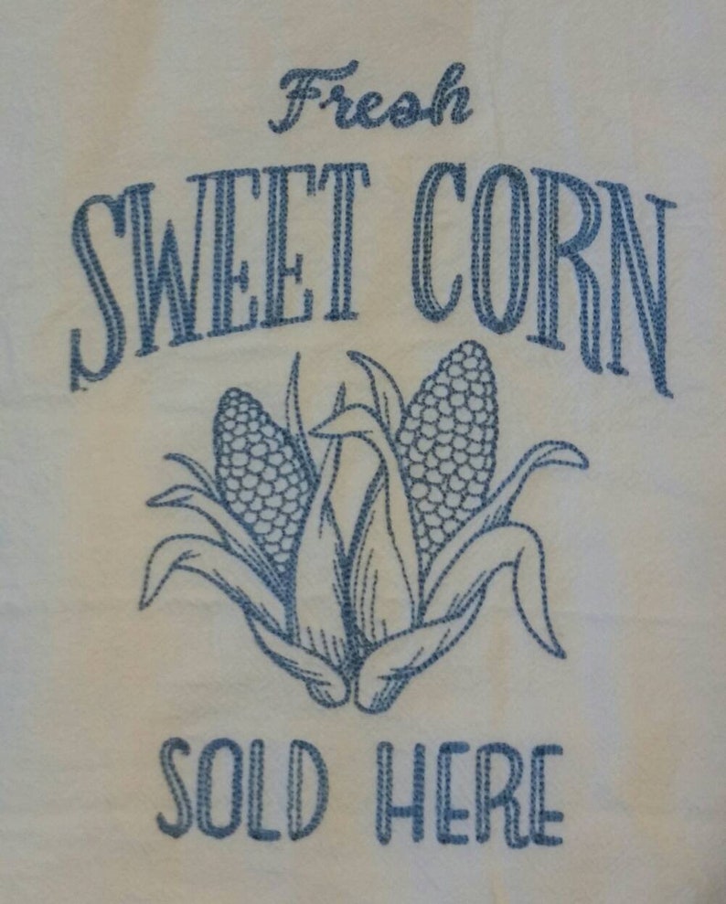 May include: White kitchen towel with blue embroidery that reads "Fresh Sweet Corn Sold Here". The embroidery also includes a depiction of three ears of corn.