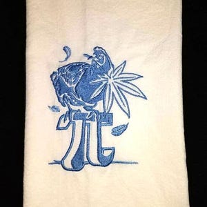 May include: A white tea towel with a blue embroidered design of a bird perched on a stylized letter 'T'.