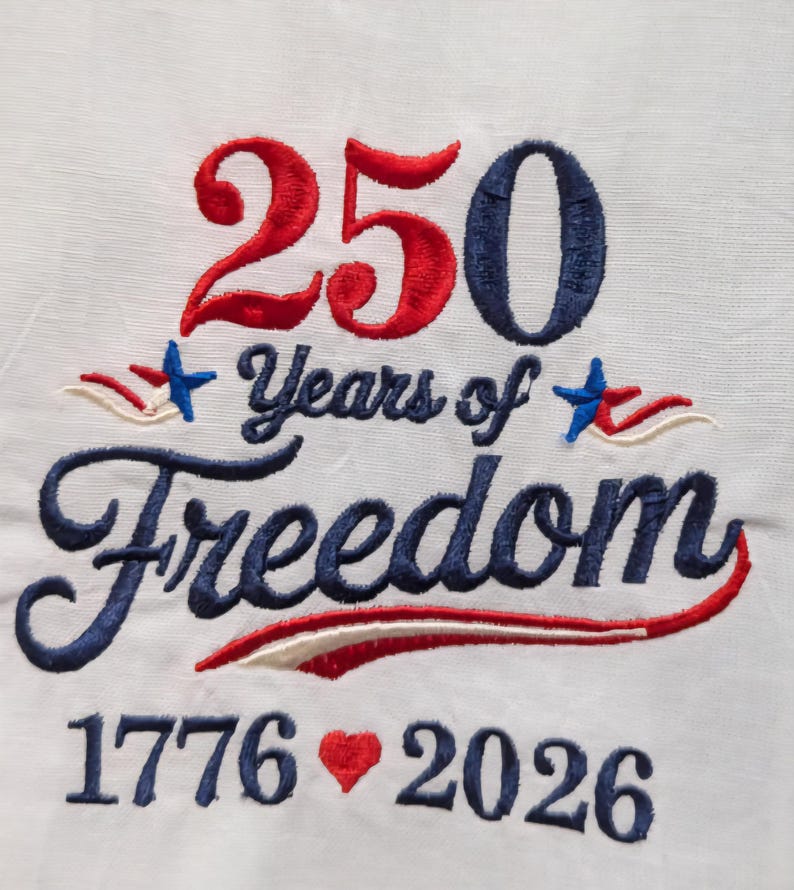 May include: White fabric embroidered with the text "250 Years of Freedom" in red and blue thread. The numbers "250" are in red and blue, with the years "1776" and "2026" below. A red heart is embroidered between the years.
