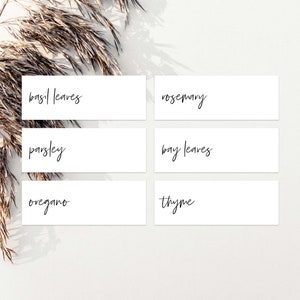 May include: Six white rectangular labels with handwritten names of herbs: basil leaves, rosemary, parsley, bay leaves, oregano, and thyme.