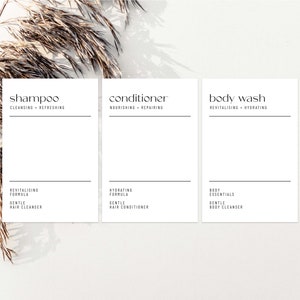 Könnte beinhalten: Drei minimalistische weiße Etiketten für Badprodukte: Shampoo, Conditioner und Duschgel. Jedes Etikett hat schwarzen Text mit Produktnamen und Beschreibungen. Auf dem Shampoo-Etikett steht "Cleansing + Refreshing". Auf dem Conditioner-Etikett steht "Nourishing + Repairing". Auf dem Duschgel-Etikett steht "Revitalising + Hydrating".