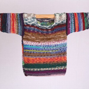 Könnte beinhalten: Ein bunter gestreifter Strickpullover mit langen Ärmeln. Der Pullover ist aus verschiedenen Farben gefertigt, darunter Rot, Orange, Gelb, Grün, Blau, Lila und Braun.