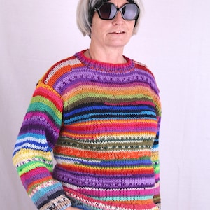 Könnte beinhalten: Eine Frau trägt einen bunten gestreiften Pullover mit einem schwarzen Stirnband und einer Sonnenbrille. Der Pullover hat eine Vielzahl von Farben, darunter Rot, Orange, Gelb, Grün, Blau, Lila und Weiß.