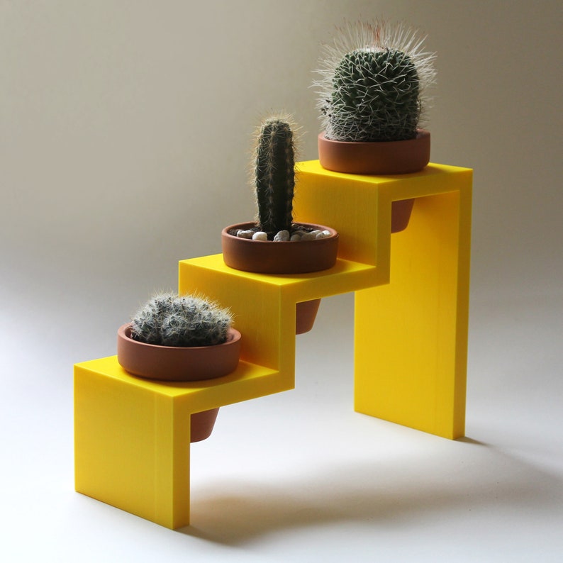 May include: A yellow, three-tiered plant stand with three potted cacti. The stand is made of plastic and has a modern design.